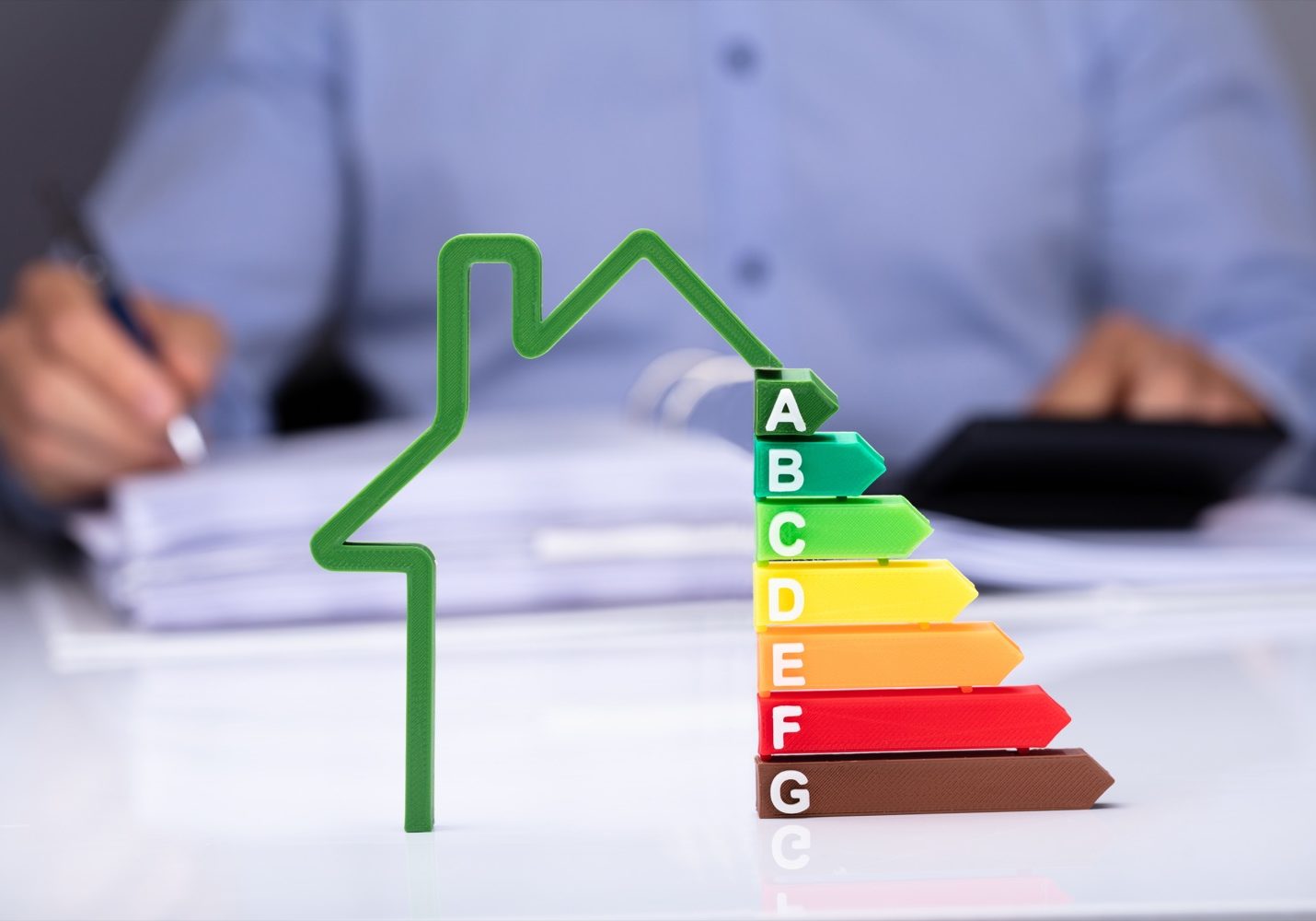 House With Energy Efficiency Rate In Front Of Businesspeople Working On Documents
